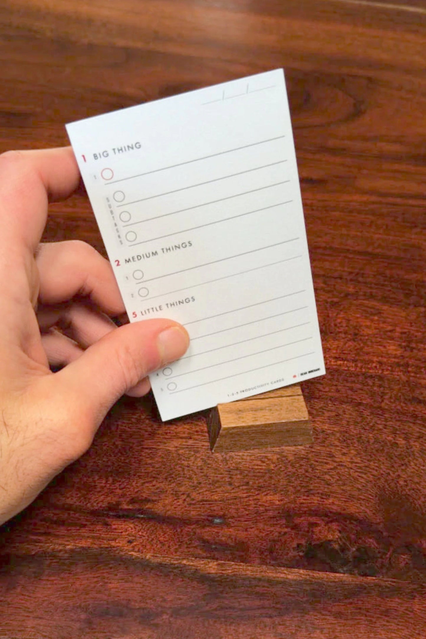 Hand holding a 1-2-5 Productivity Card on a wooden surface