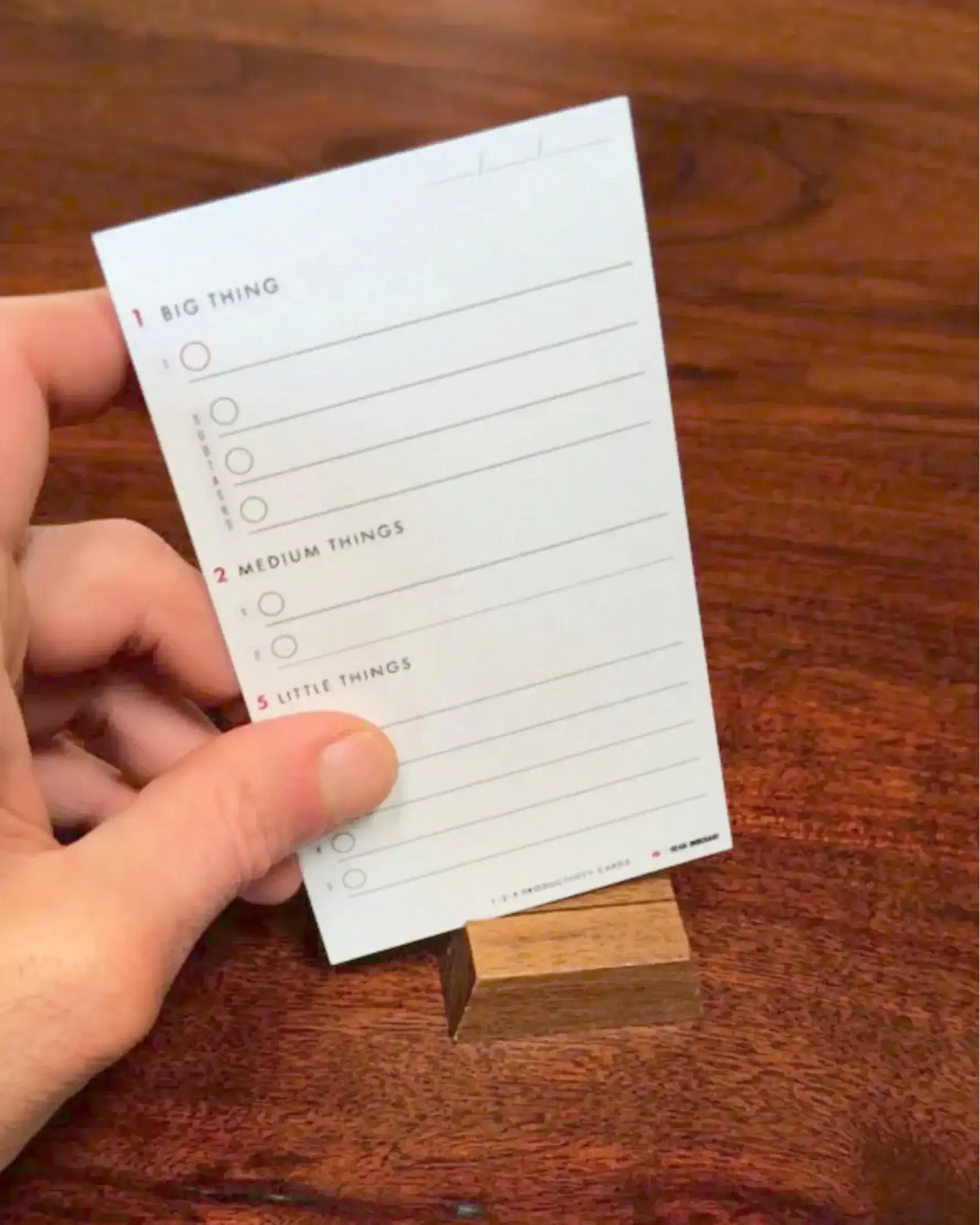 Hand holding a 1-2-5 Productivity Card on a wooden surface