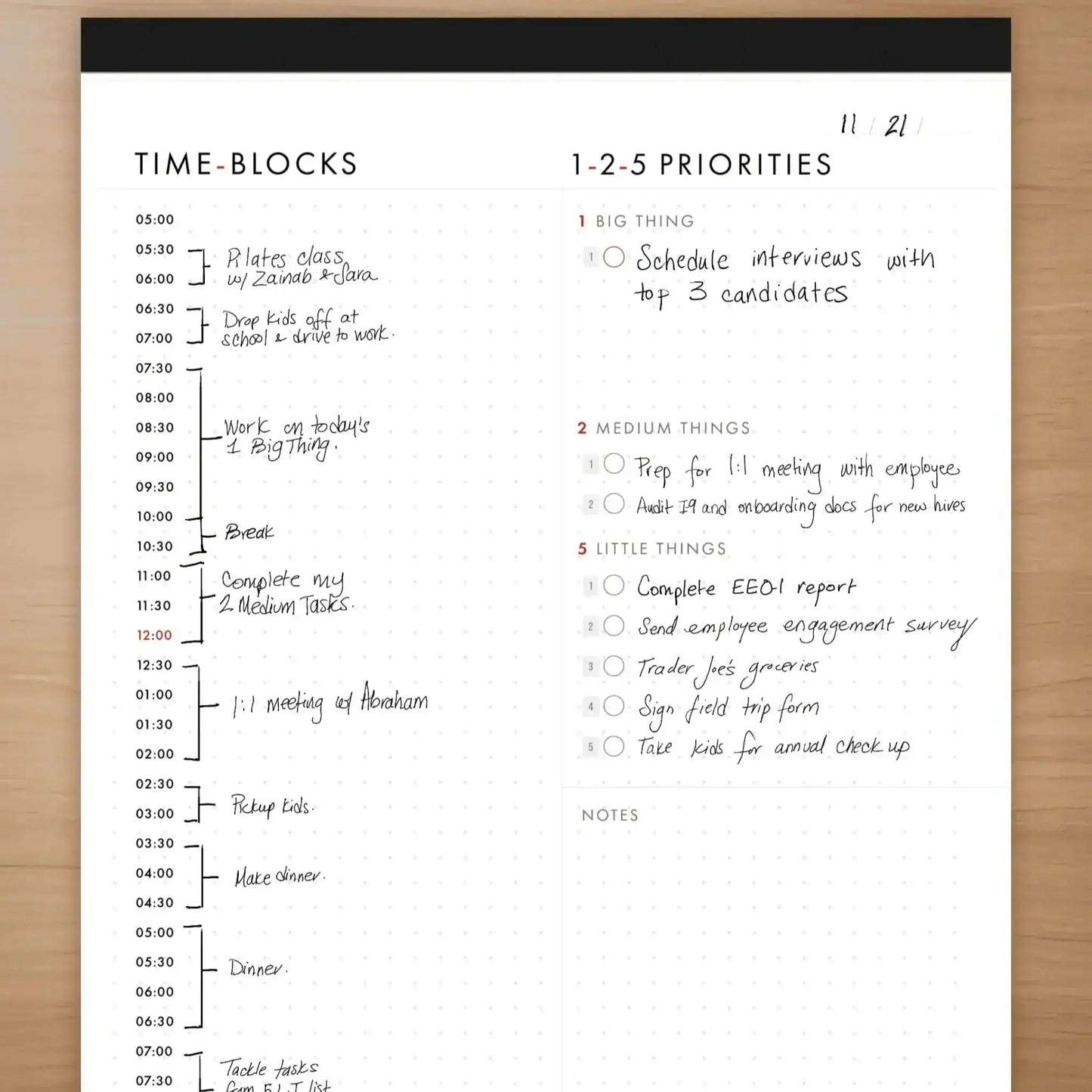 Time-blocks and priorities schedule on a white sheet with black border, placed on a wooden surface.