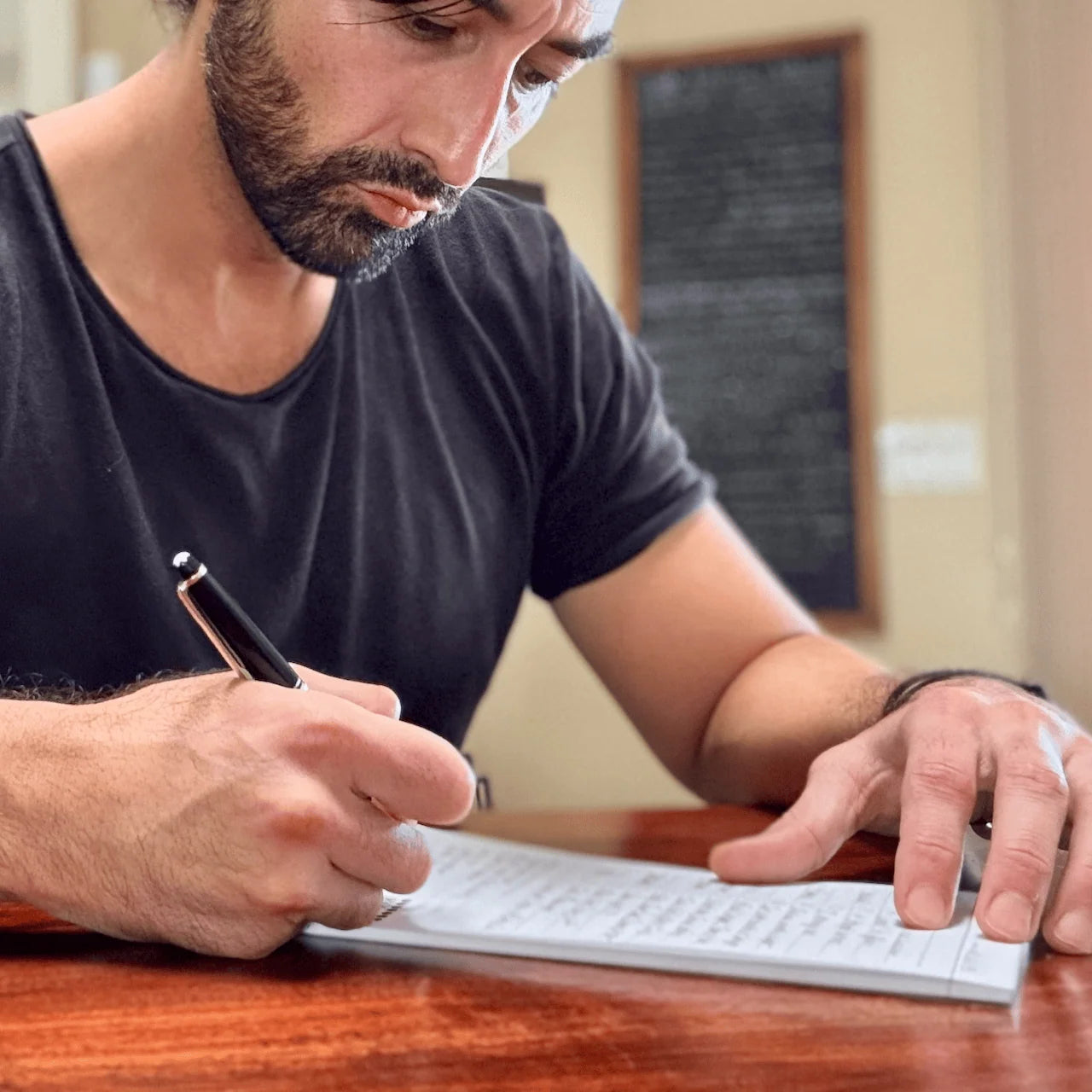 Dean Bokhari writing in a notebook with a pen on a wooden table.