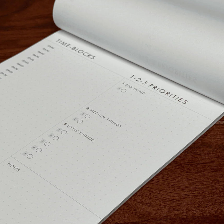 Open planner with time-blocks and priorities on a wooden surface