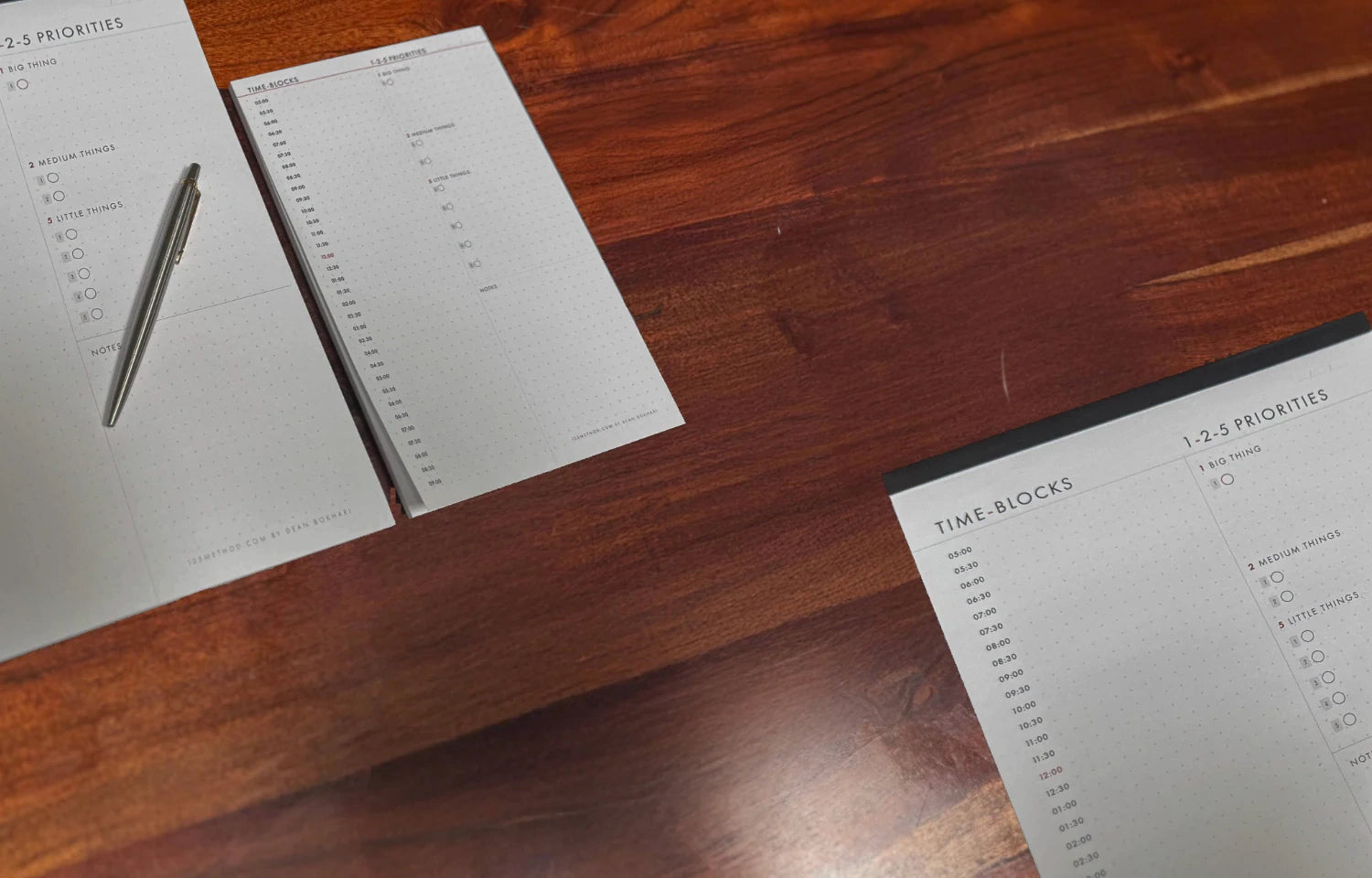 1-2-5 Time Block Planner in two sizes with a pen on a wooden surface