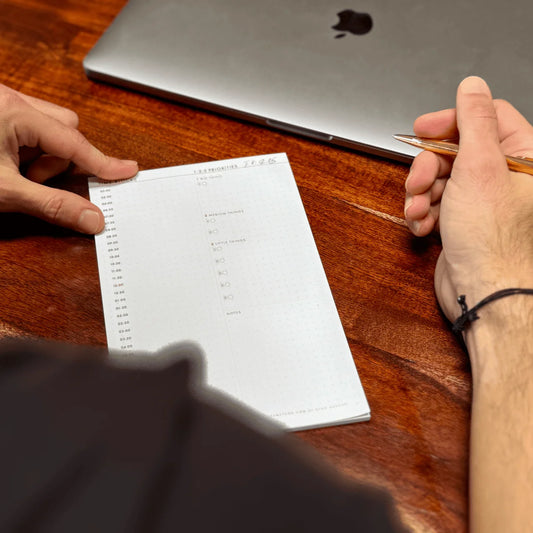 Dean Bokhari holding a pen and looking at a notepad on a wooden desk with a laptop in the background.