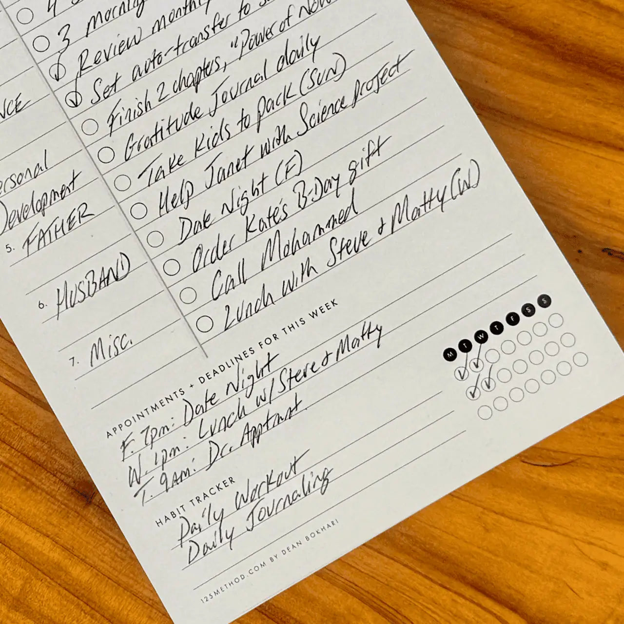 Weekly Roles and Goals Planner Pad with handwritten tasks and appointments on a wooden surface