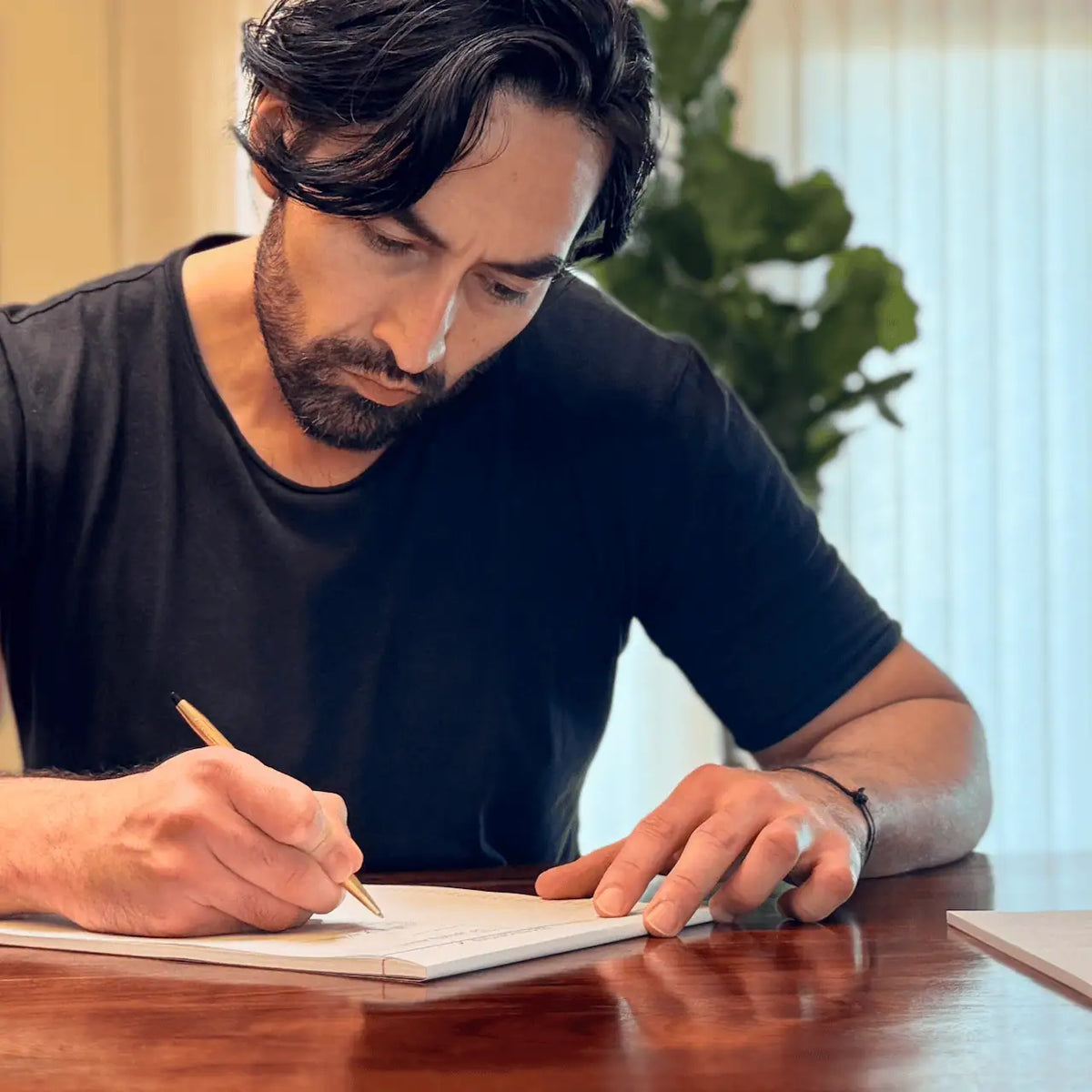 Dean Bokhari writing in the 1-2-5 Time Block Planner at a table with a blurred indoor background