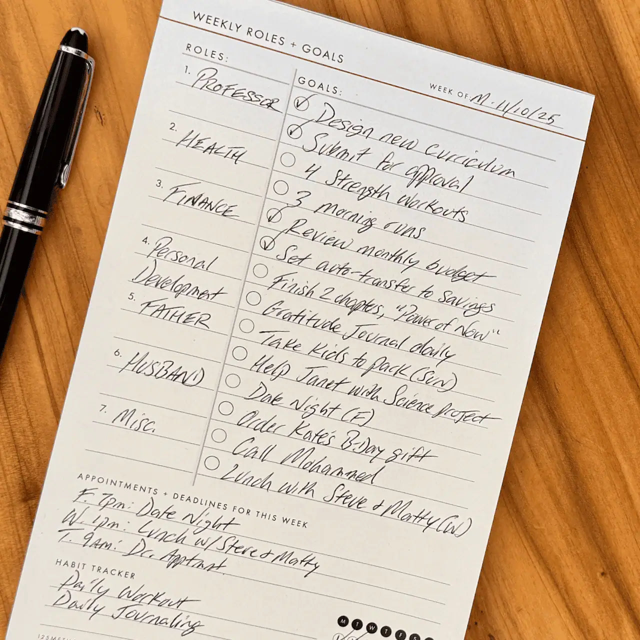 Weekly Roles and Goals Planning Pad  with a pen on a wooden table